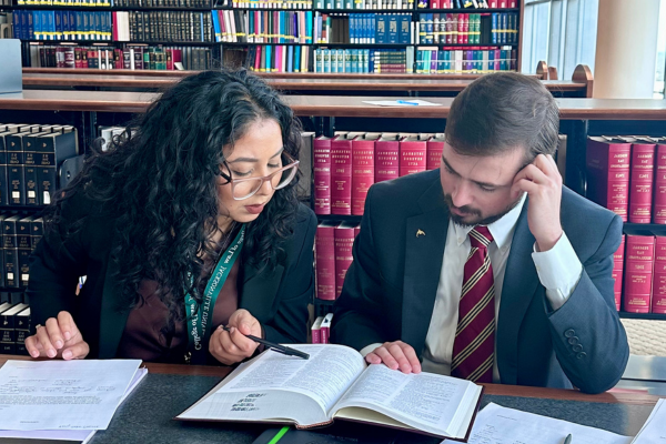 Two students reading a law textbook together in a legal library.